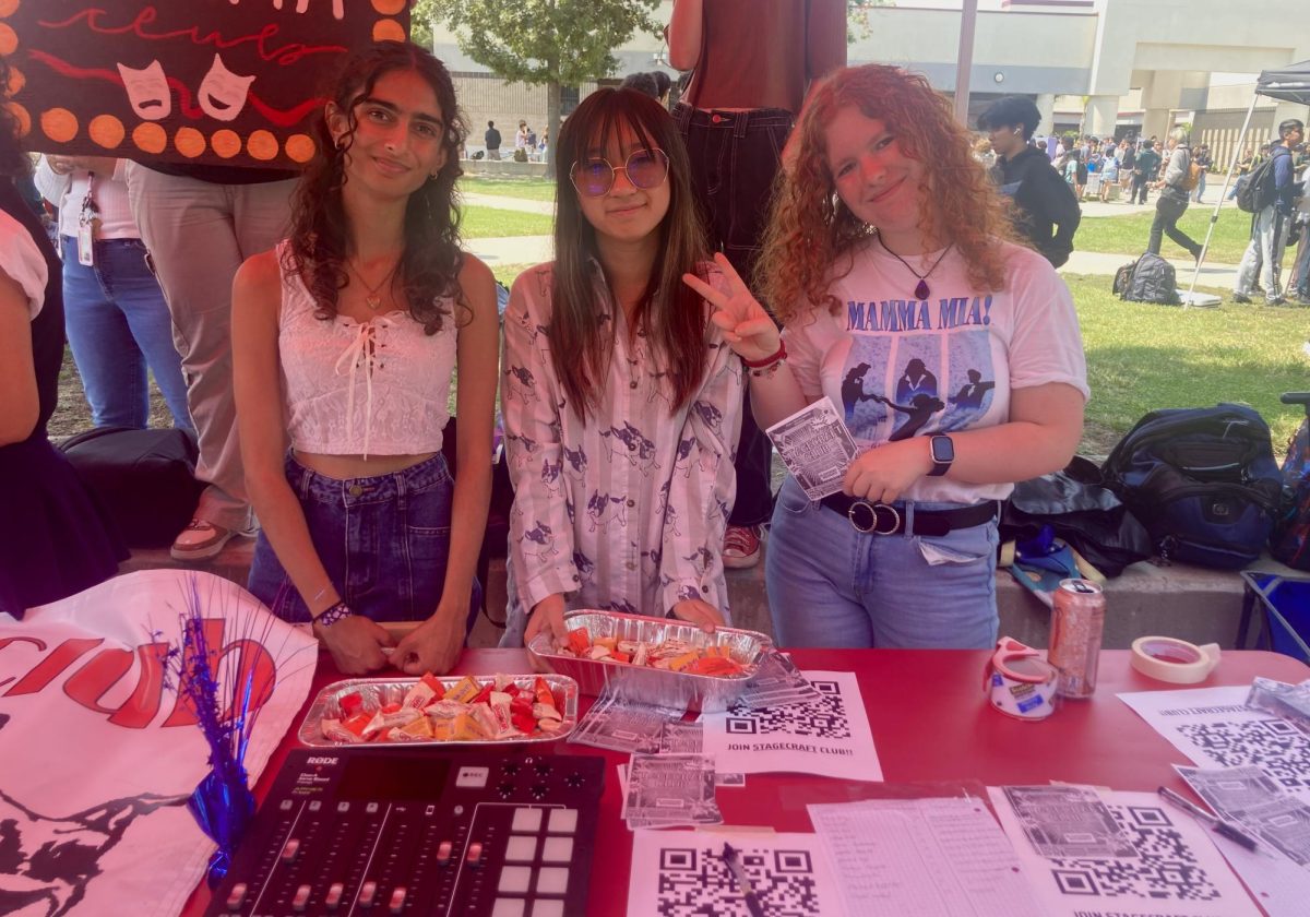 Stage Craft club officers set up a table with treats and a soundboard, demonstrating to passing students their essential role in creating sound effects for theater productions. From left to right: Devi Bhatt (12), Natalie Derona (12), and Jasmine Houde (12).