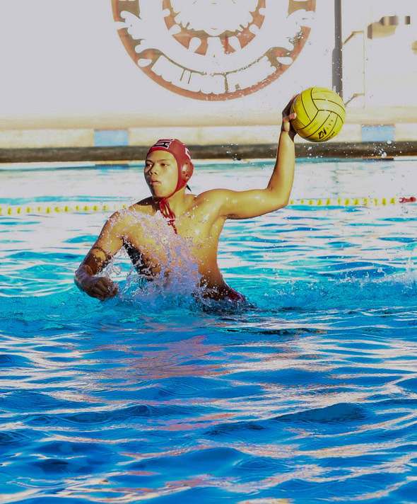 Varsity senior Kai Santiago rising through the water wielding the ball, preparing to take a shot.
